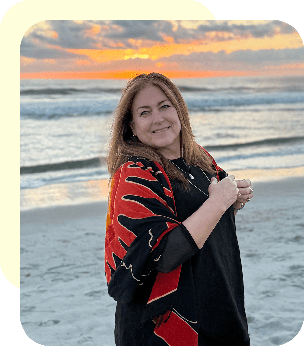 Woman smiling by the beach at sunset, wrapped in a colorful shawl.