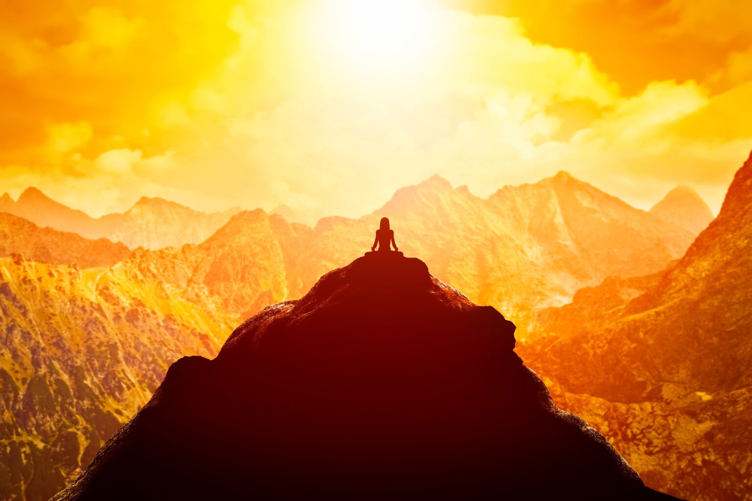 Silhouette of a person meditating atop a mountain during a vibrant sunrise.