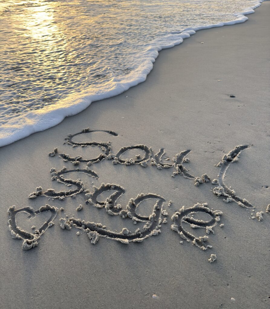Words 'Soul & Sage' written in the sand by the ocean.