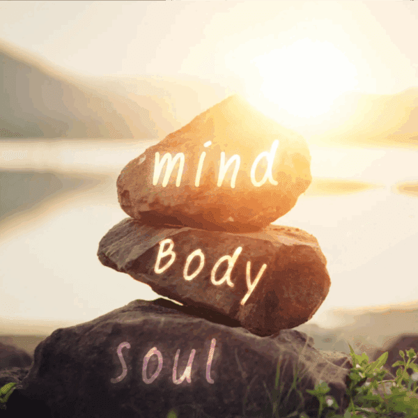 Stacked stones labeled mind, body, soul at sunrise by water.