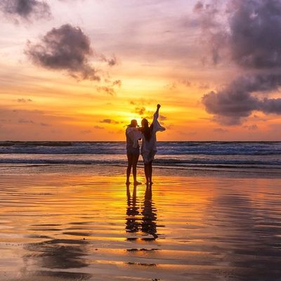 Couple enjoying a vibrant sunset on the beach, reflecting on wet sand.