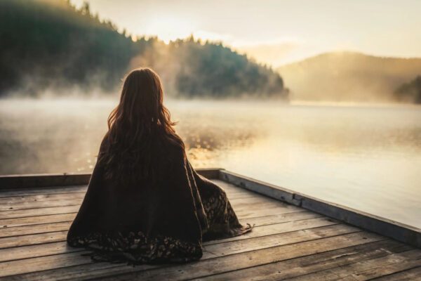 A person sitting on a dock overlooking a misty lake at sunrise.