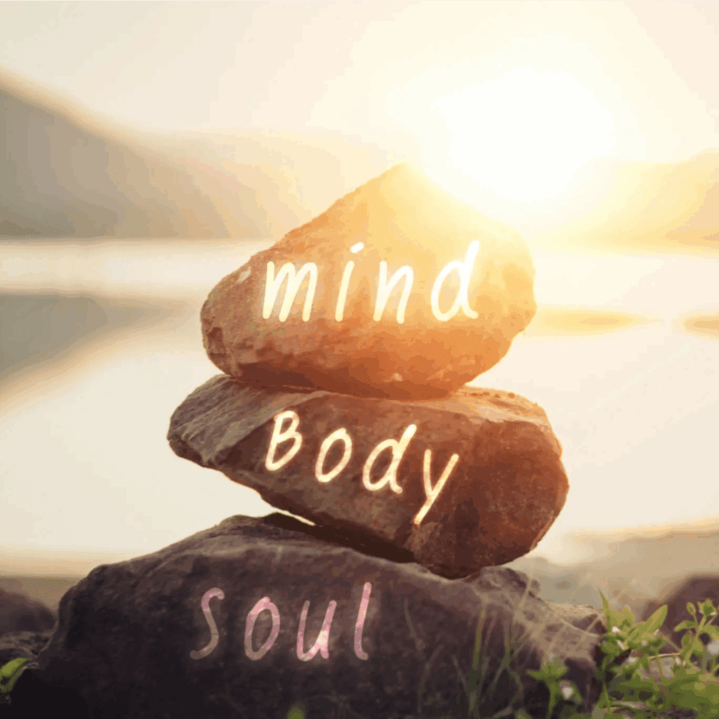 Stacked stones labeled mind, body, soul at sunrise by water.